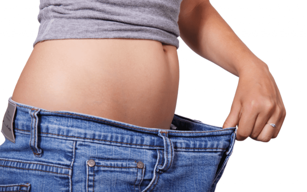 Eine Frau zeigt wieviel sie abgenommen hat indem sie eine Hose von vor ihrer Paleo Diet an hat.